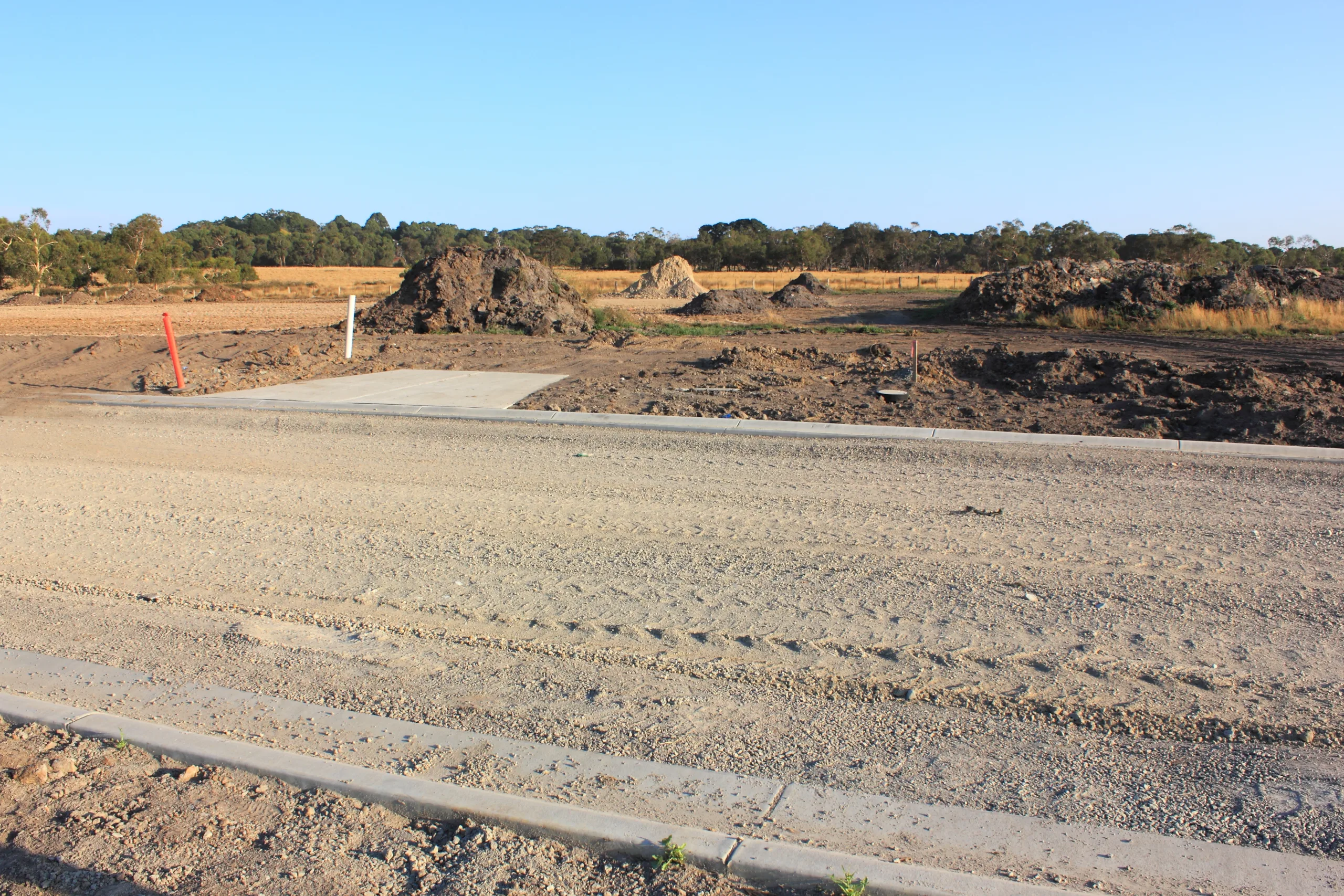 New,Land,Subdivision,In,Suburbia,With,Work,On,Roads,And Excavator loading soil into a dump truck at a construction site.